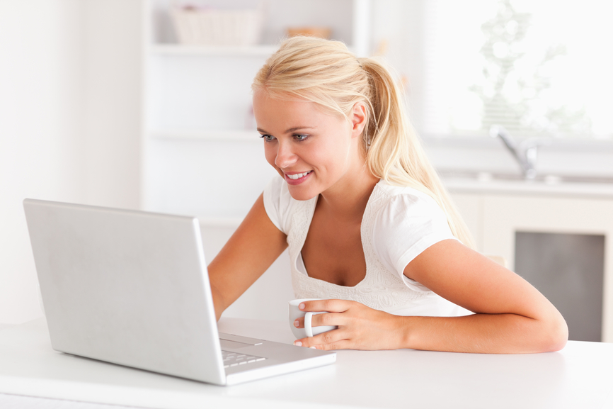 Cute woman having a cup of tea while using her notebook in her kitchen